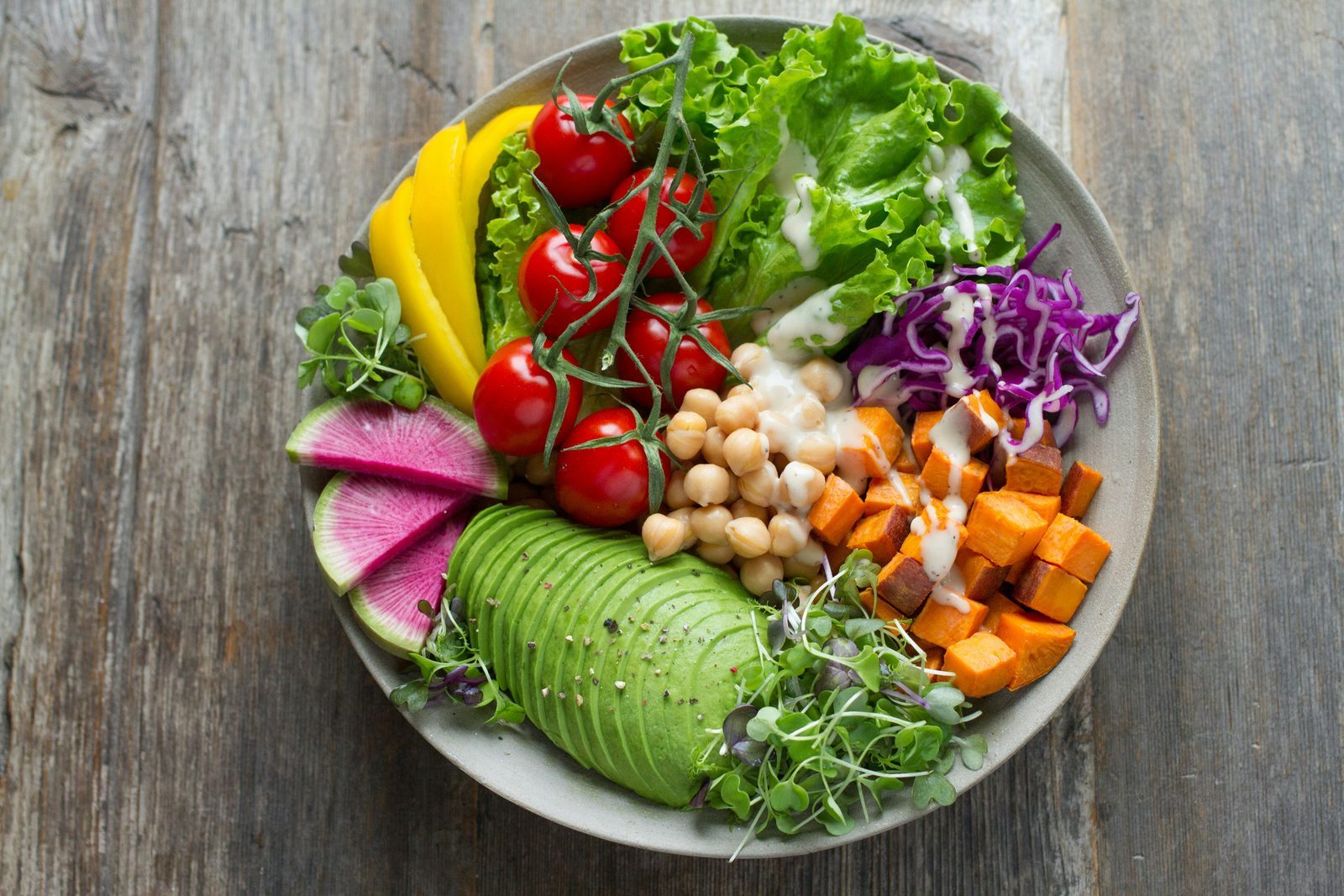Plant-rich bowl with avocado, chickpeas, sweet potato, tomatoes, greens and cabbage
